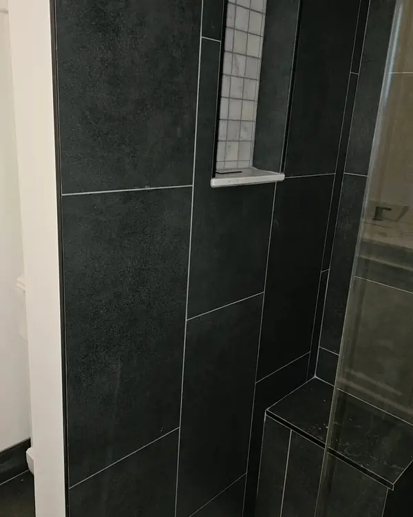 Black-tile walk-in shower with a built-in bench and frameless glass