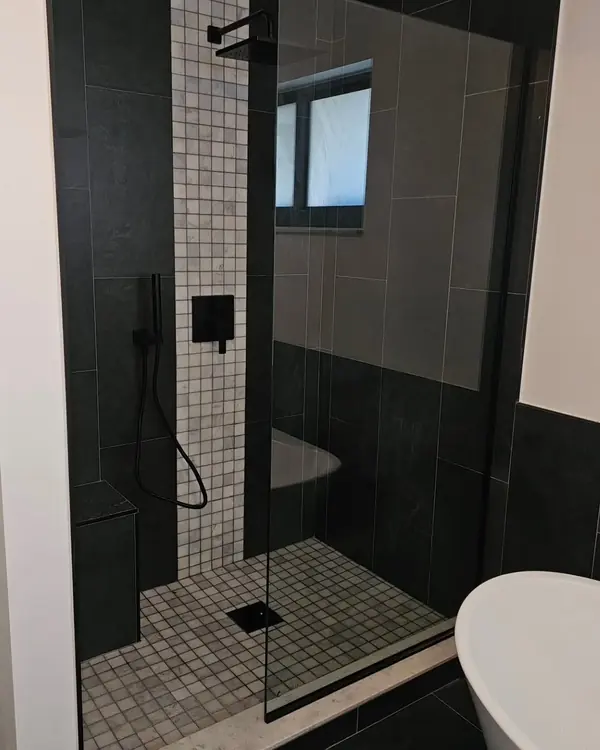 Walk-in shower with black tile, frameless glass, black fixtures and a white mosaic floor