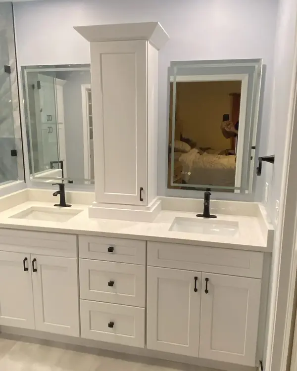 Double vanity with a center tower cabinet, black faucets and lit mirrors
