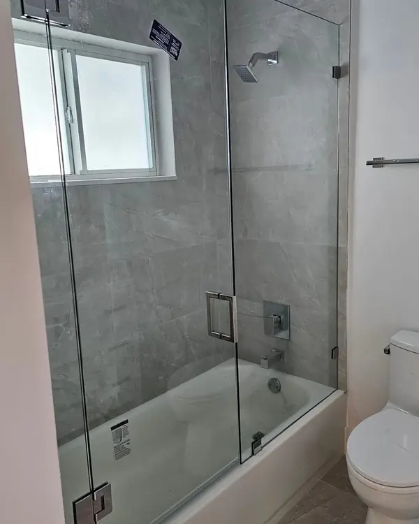 Bathtub with a frameless glass panel and grey tile walls