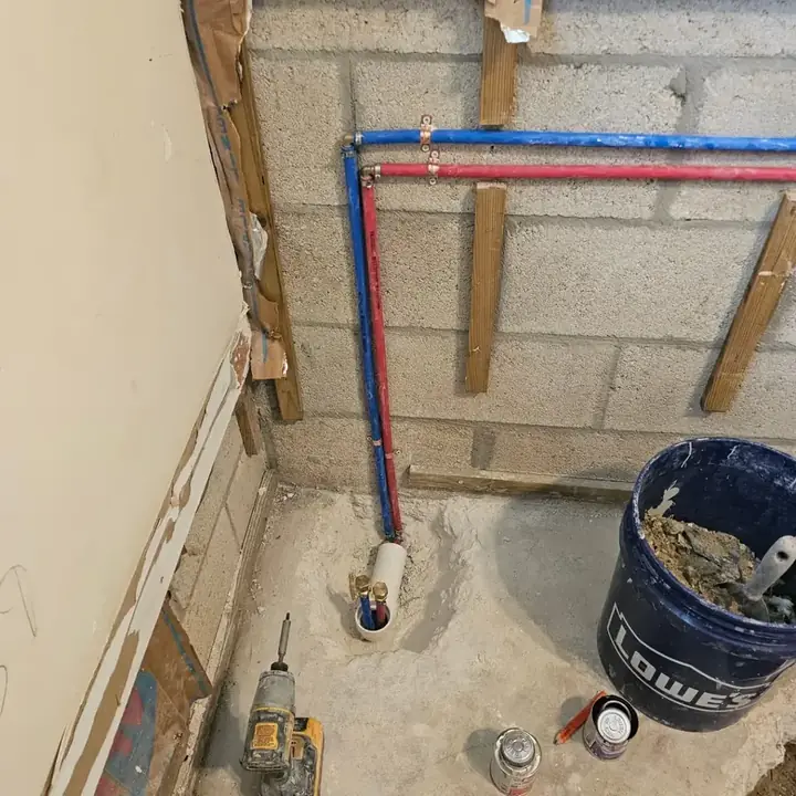 Bathroom wall opened down to the block, with new red and blue water lines run along it