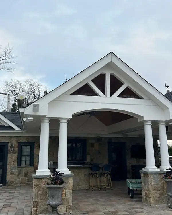 Covered front porch with a gable roof and white columns on a stone house