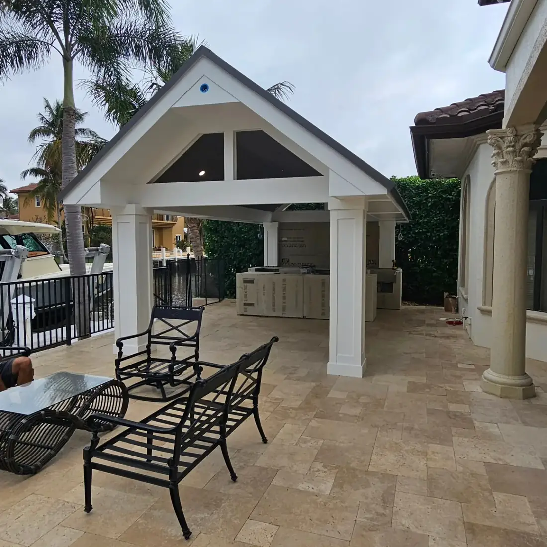 Finished pavilion with a white gable roof, square white columns and a finished ceiling over a travertine patio