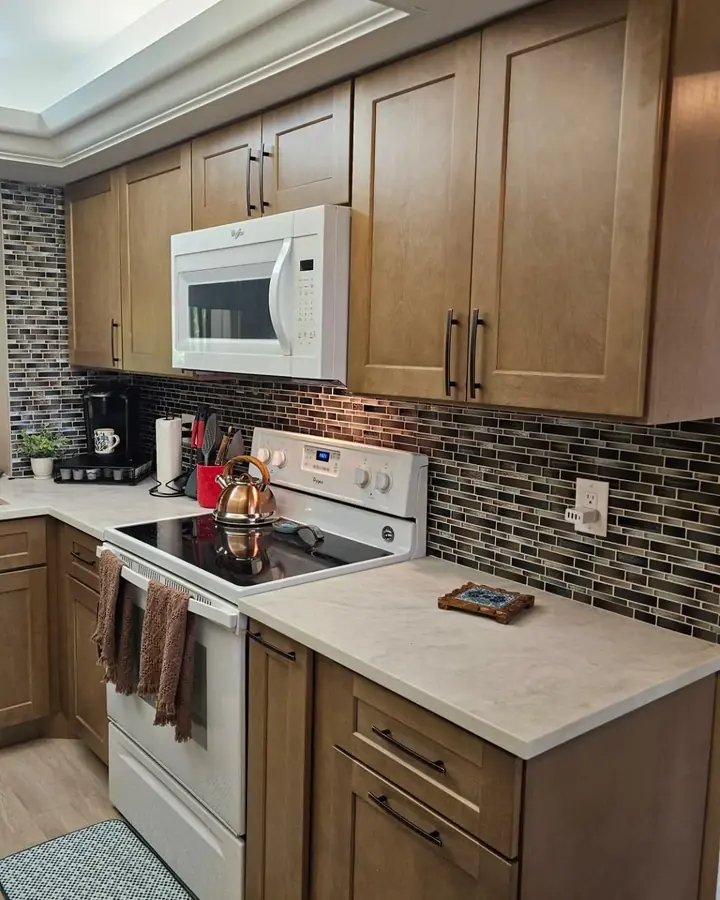 Finished kitchen with stained shaker cabinets, a glass mosaic backsplash and light countertops