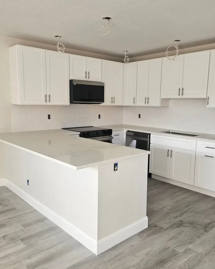 Finished white kitchen with shaker cabinets, white countertops, a peninsula and grey plank floors