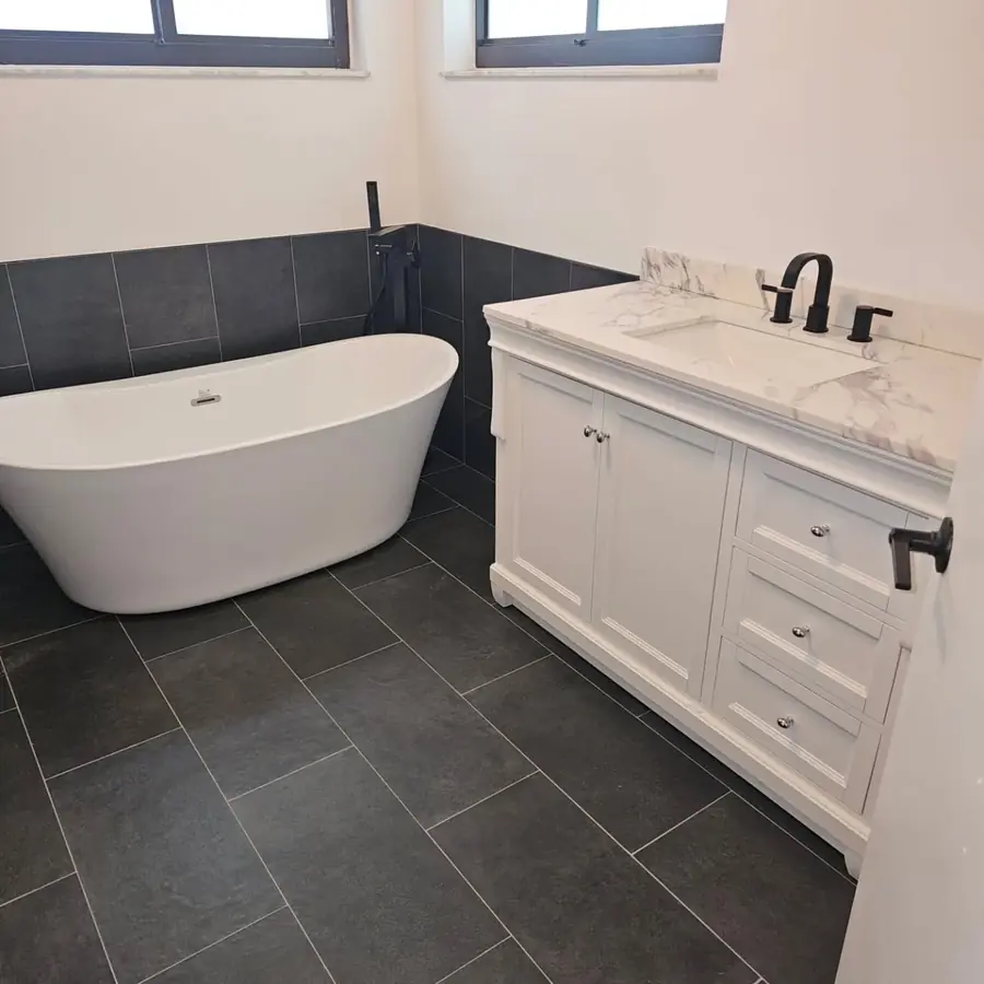 Finished bathroom with a freestanding tub, a white vanity and dark tile floors