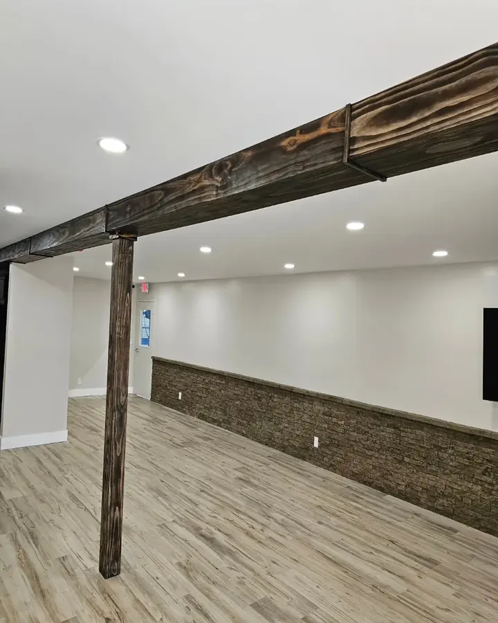 Finished room with a wood beam and post, stone-veneer wainscoting and wood-look plank floors