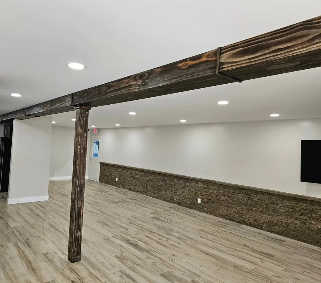Finished room with a stained wood beam and post, stacked-stone wainscoting, wood-look plank floors and recessed lights