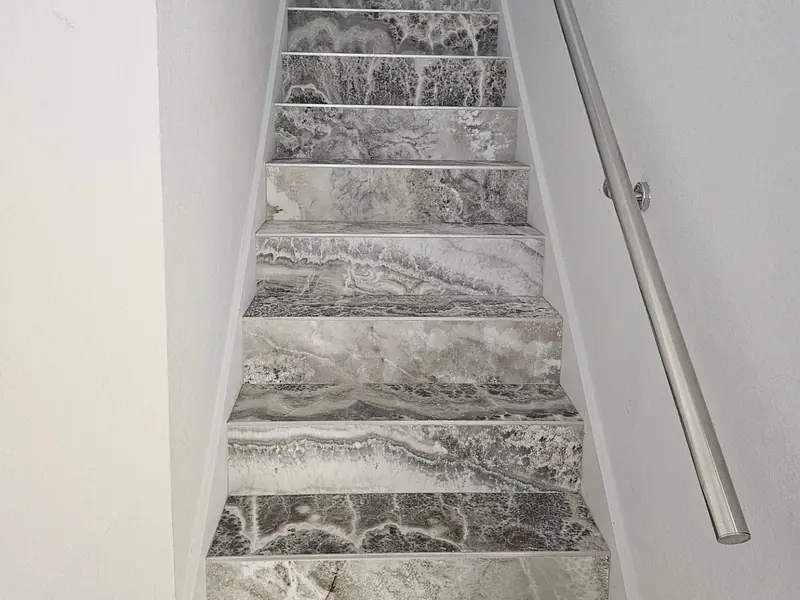 Staircase with marble-look tile treads and a steel handrail