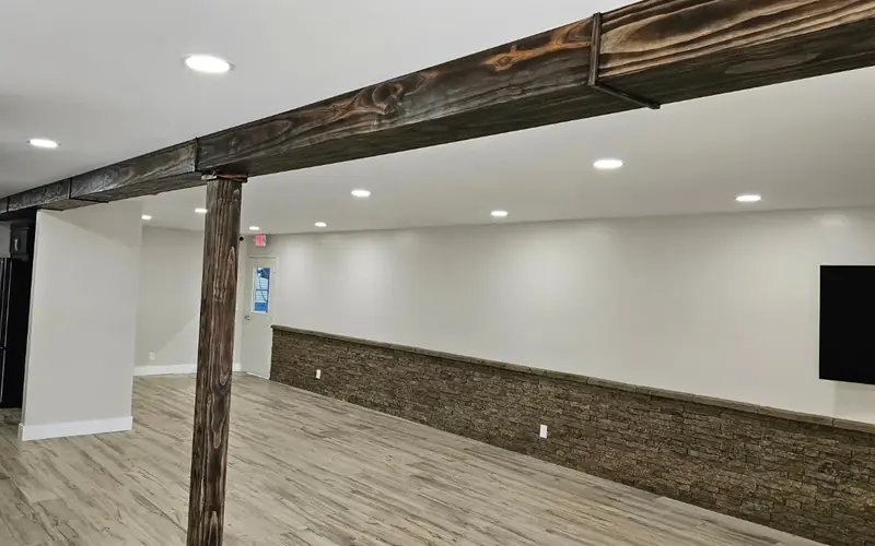 Finished room with a wood beam, stacked-stone wainscoting and plank floors