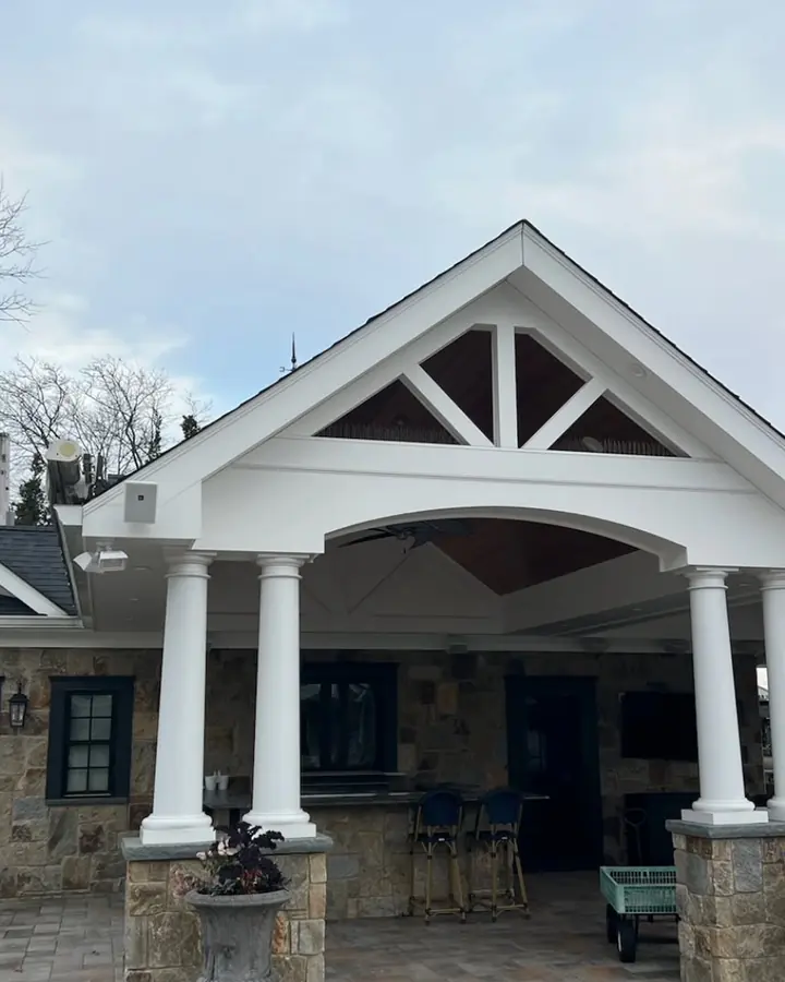 Covered front porch with a gable roof and white columns on a stone house