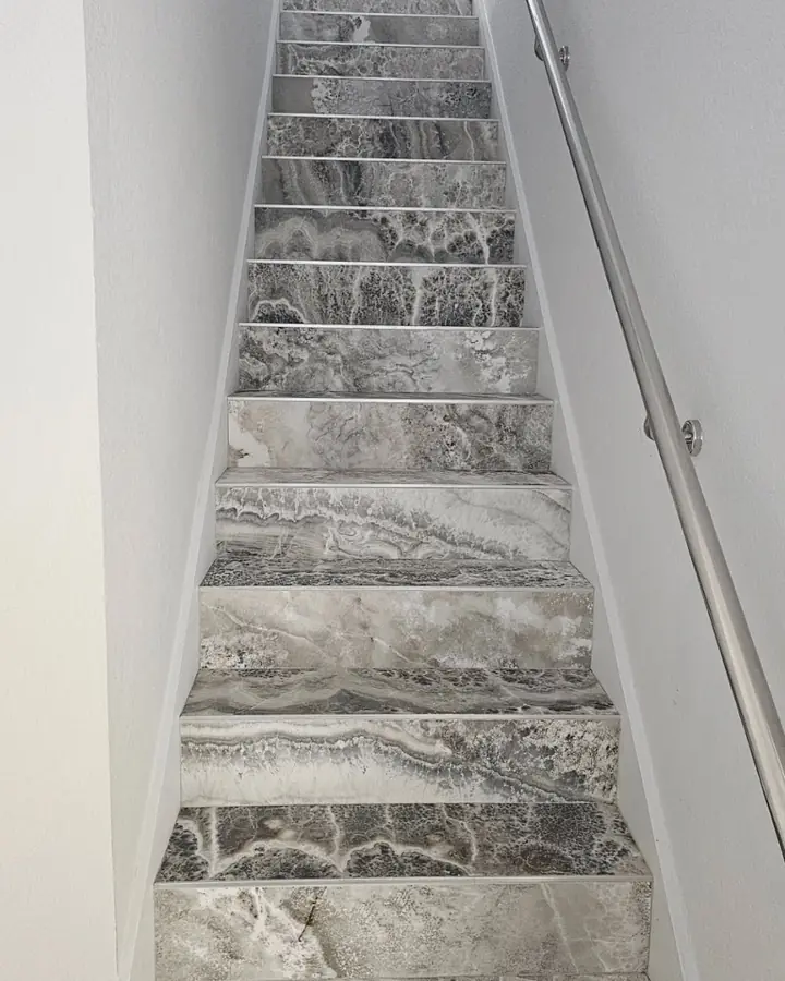 Staircase with marble-look tile treads and a steel handrail