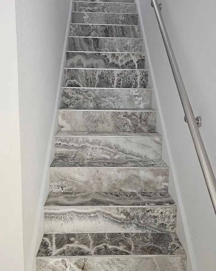 Staircase with marble-look tile treads and a steel handrail