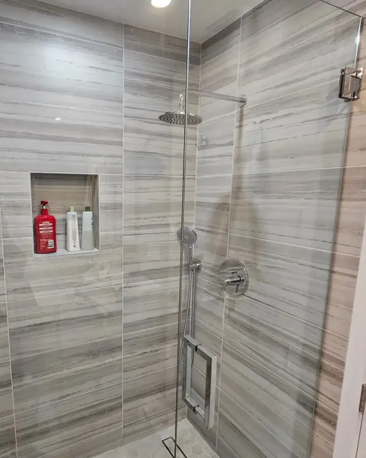 Walk-in shower with grey linear tile, a tiled niche and frameless glass