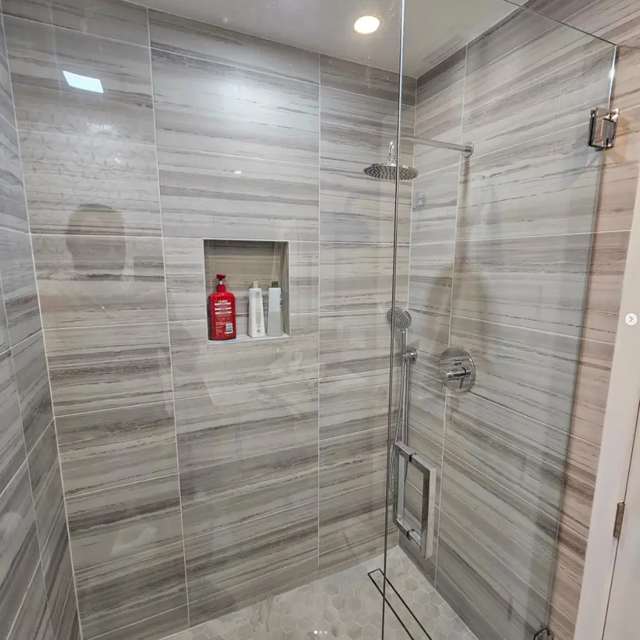 Walk-in shower with grey linear tile, a frameless glass door and a built-in niche