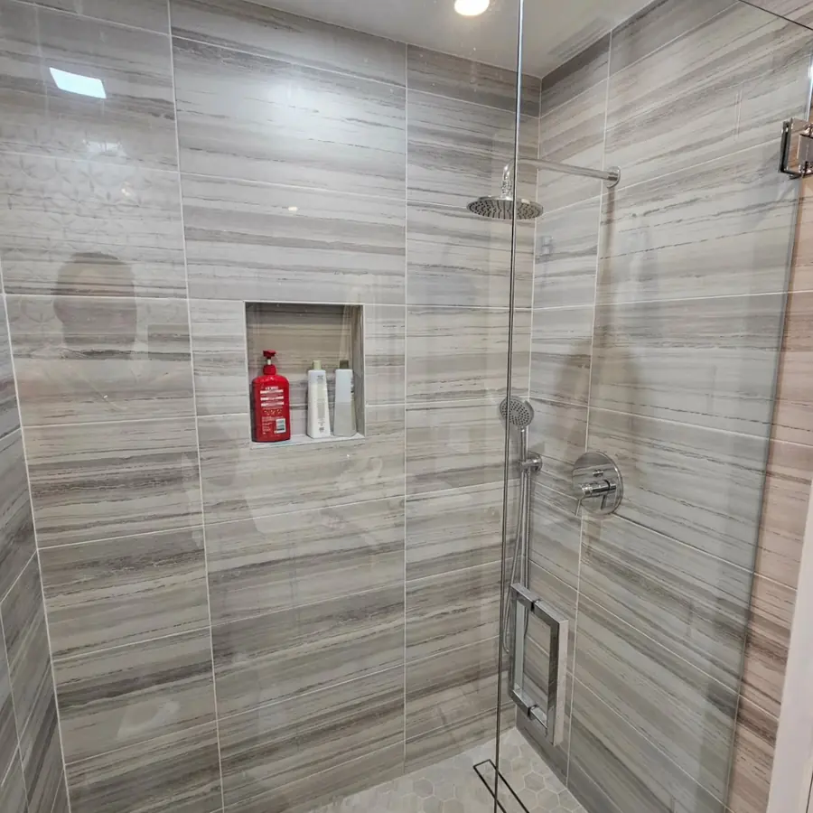 Walk-in shower with grey linear tile, a frameless glass door and a built-in niche