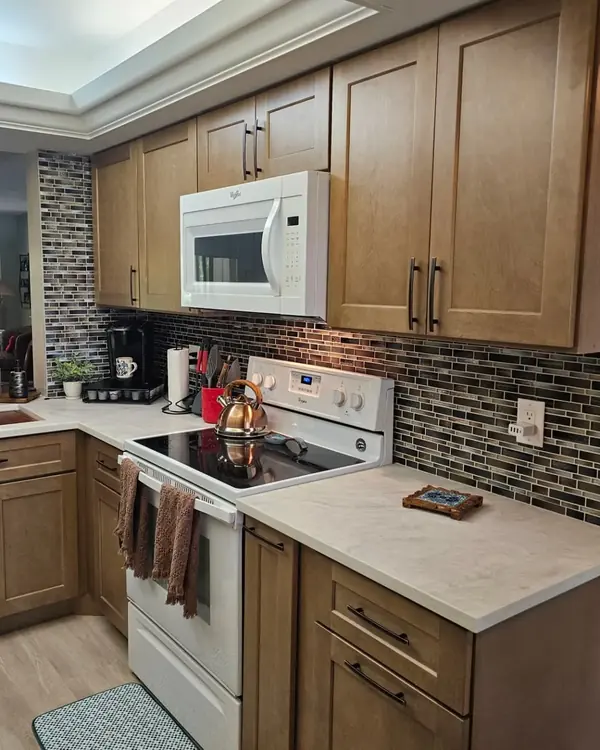 Finished kitchen with stained shaker cabinets, a glass mosaic backsplash and light countertops