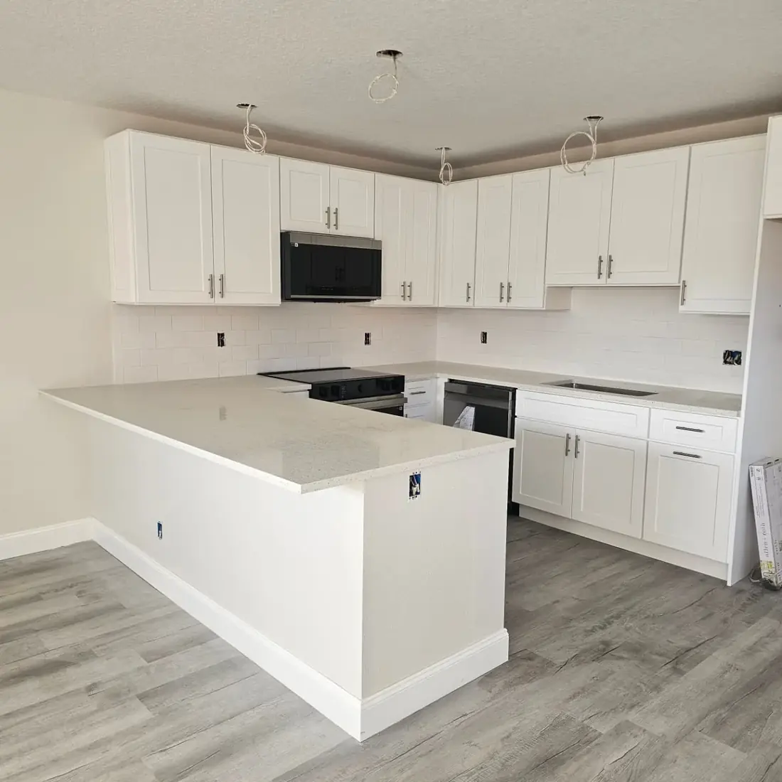 Finished white kitchen with shaker cabinets, white countertops, a peninsula and grey plank floors